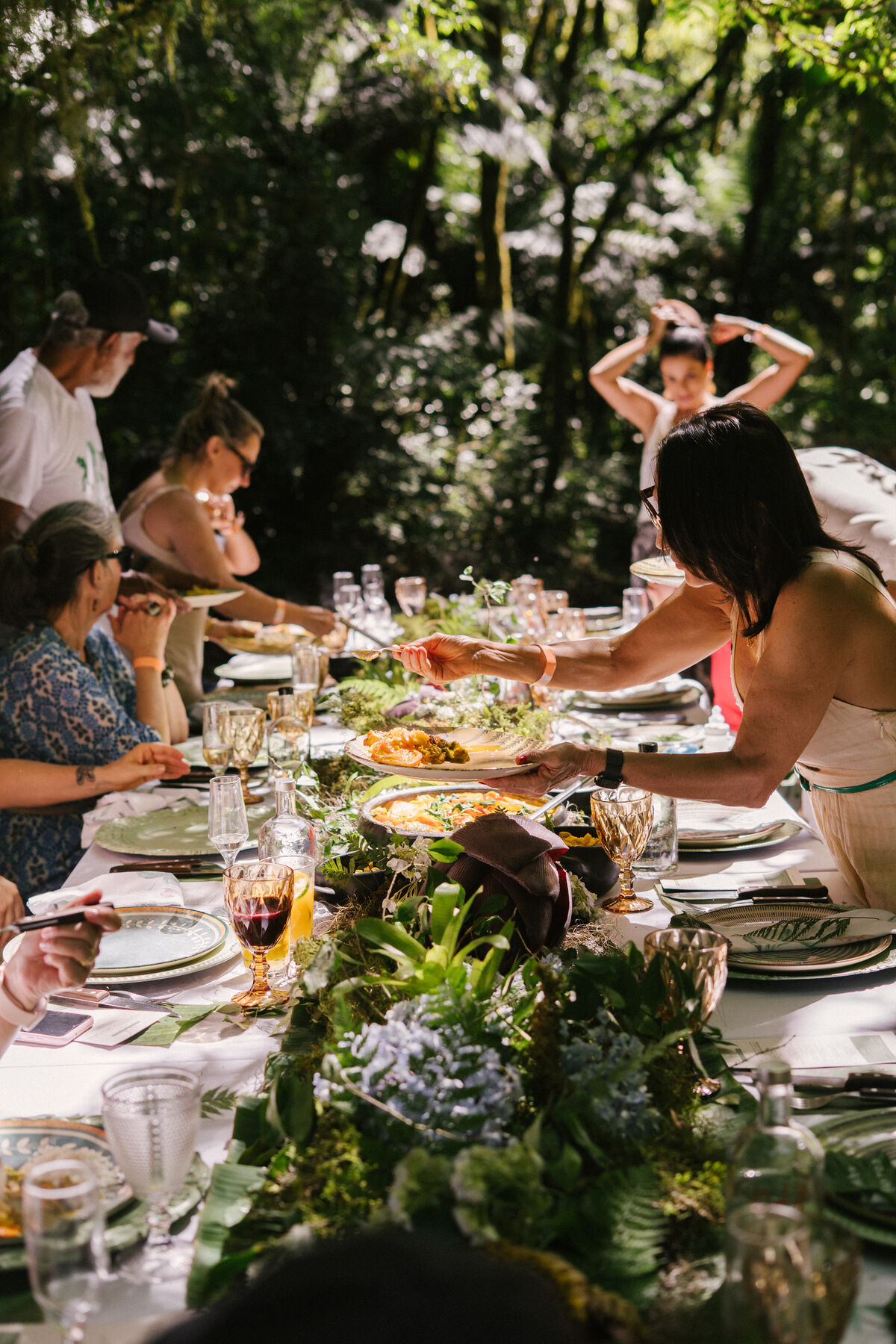 Convidados à mesa longa decorada com flores, na mata