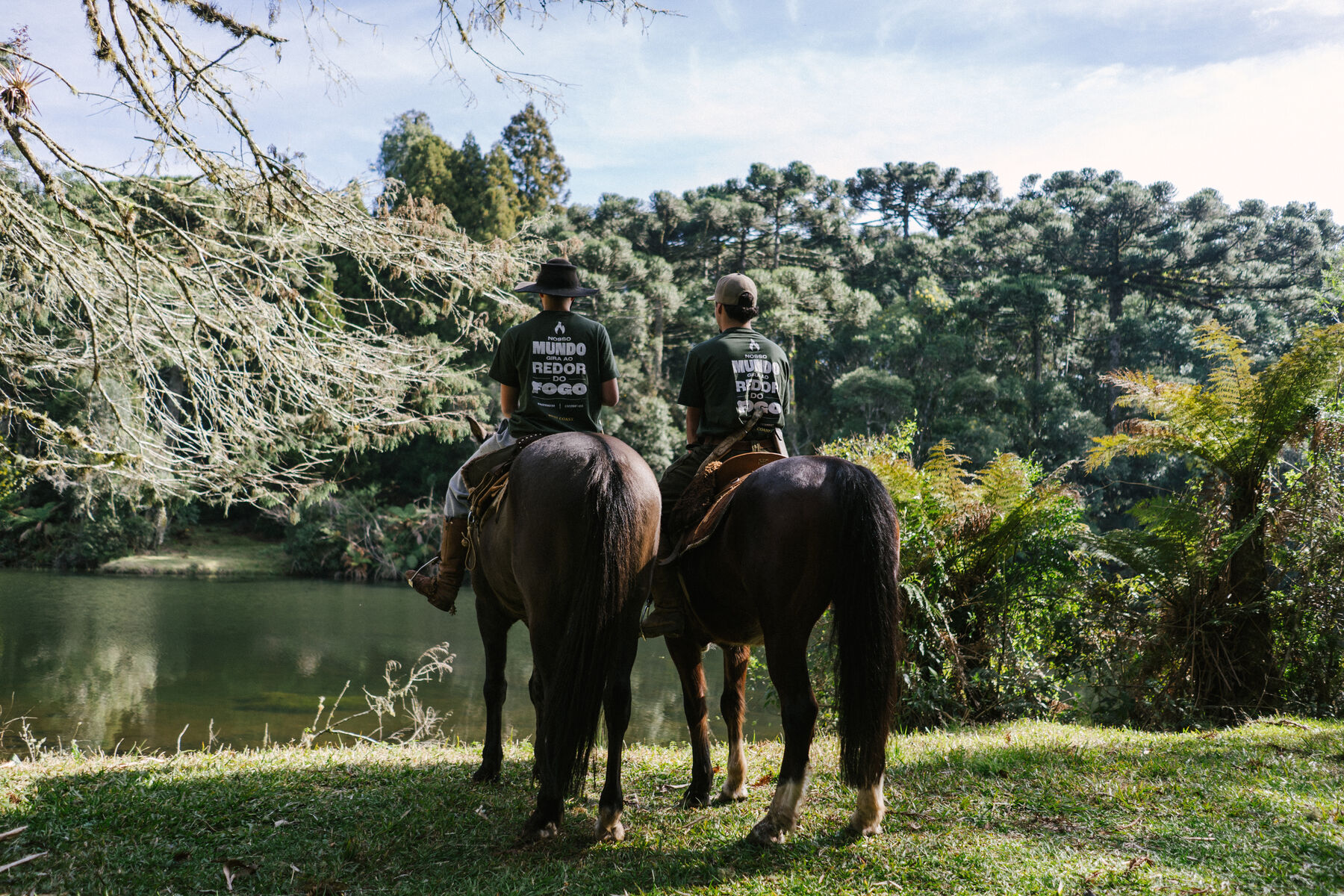 Dois cavaleiros à beira do lago, com a mata ao fundo