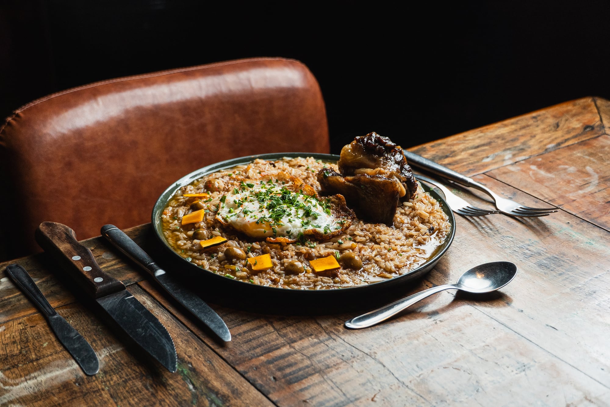 Arroz caldoso de costela com ovo, na mesa de madeira junto à cadeira de couro