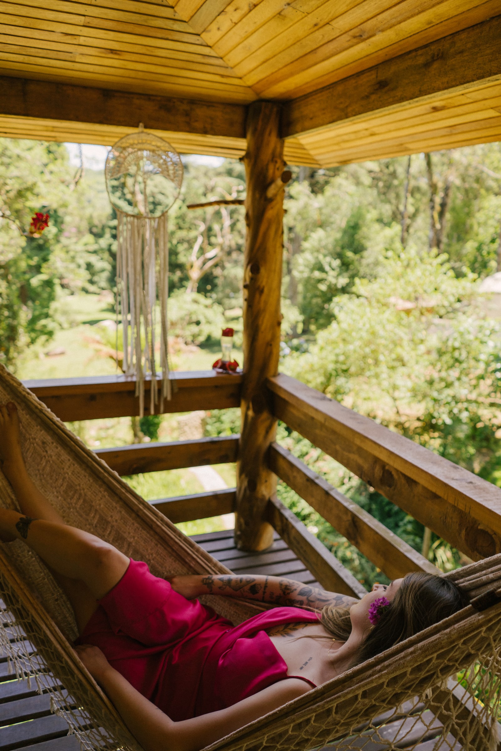 Hóspede descansando na rede da varanda de madeira, de frente para a mata